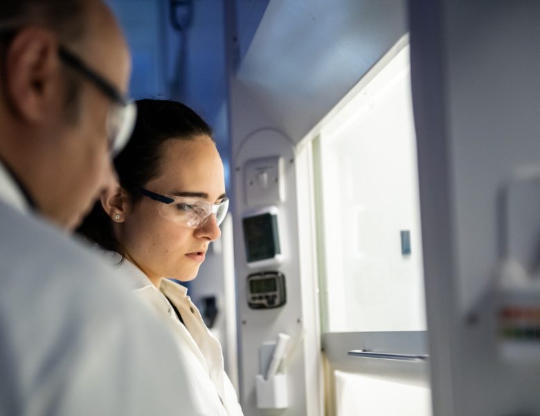 Two people at a fume cupboard in a lab